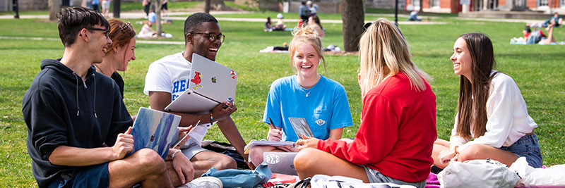 A group of students chat while sitting out on the quad.